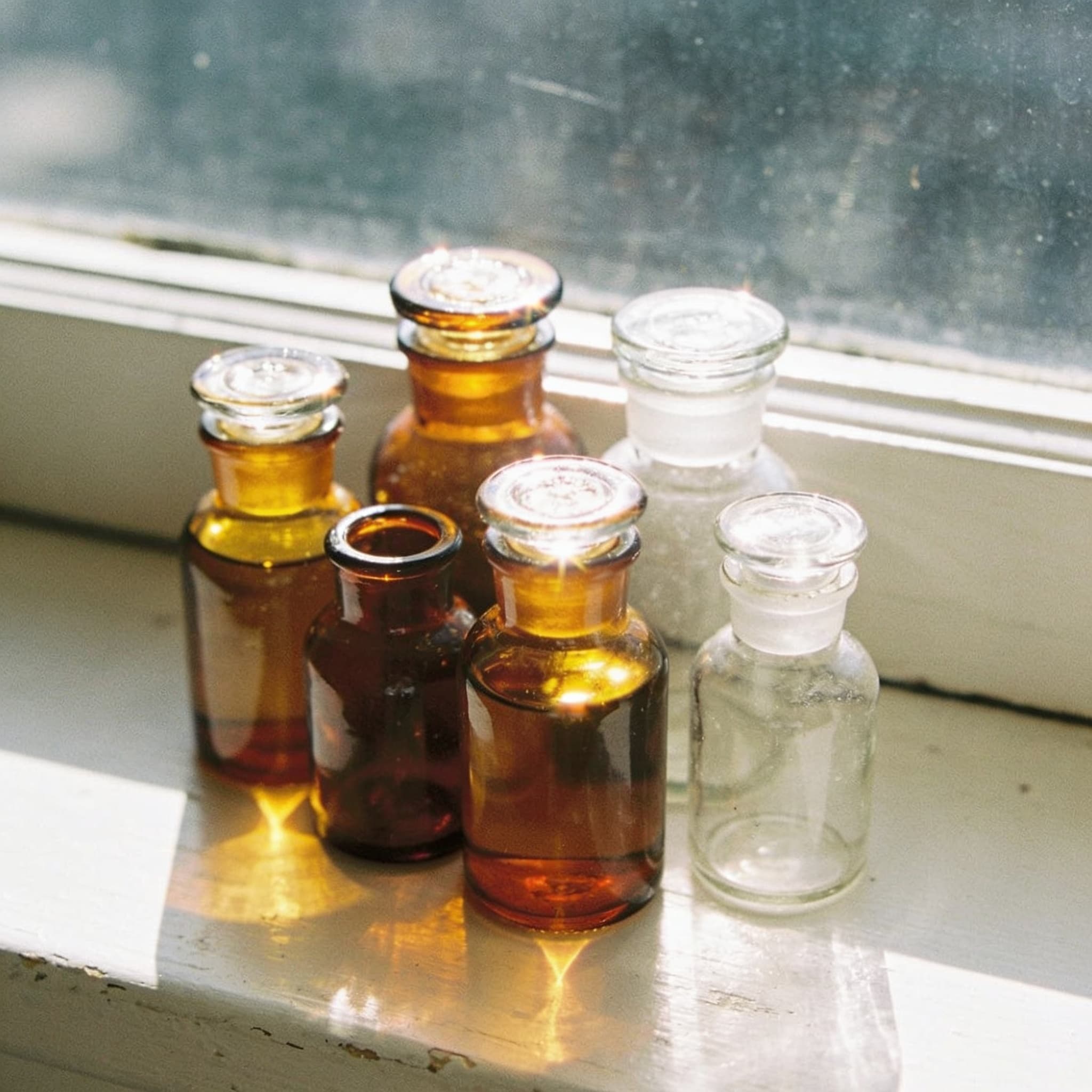 Amber and clear apothecary glass on a sunlit shelf in the studio
